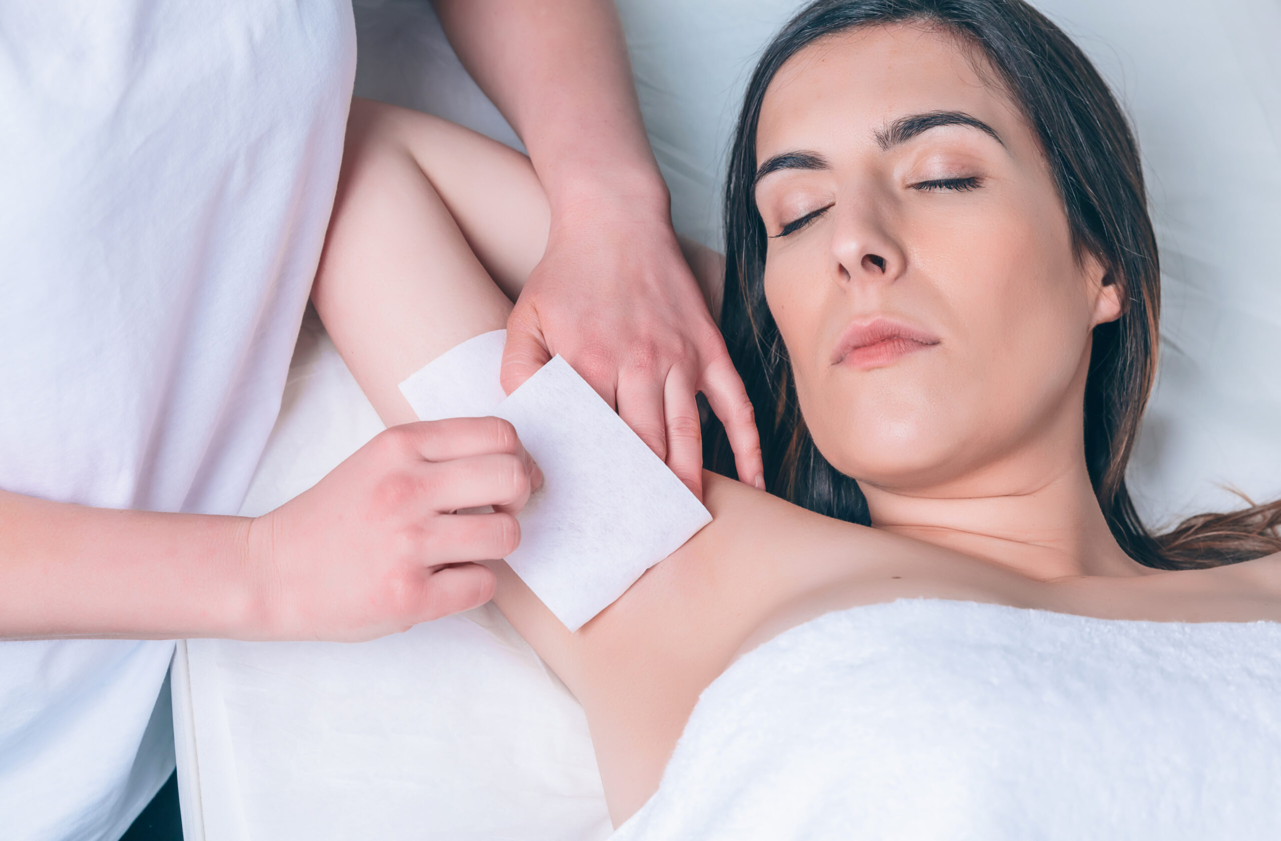 Beautician hands doing depilation armpit to beautiful woman with wax strip in a beauty salon